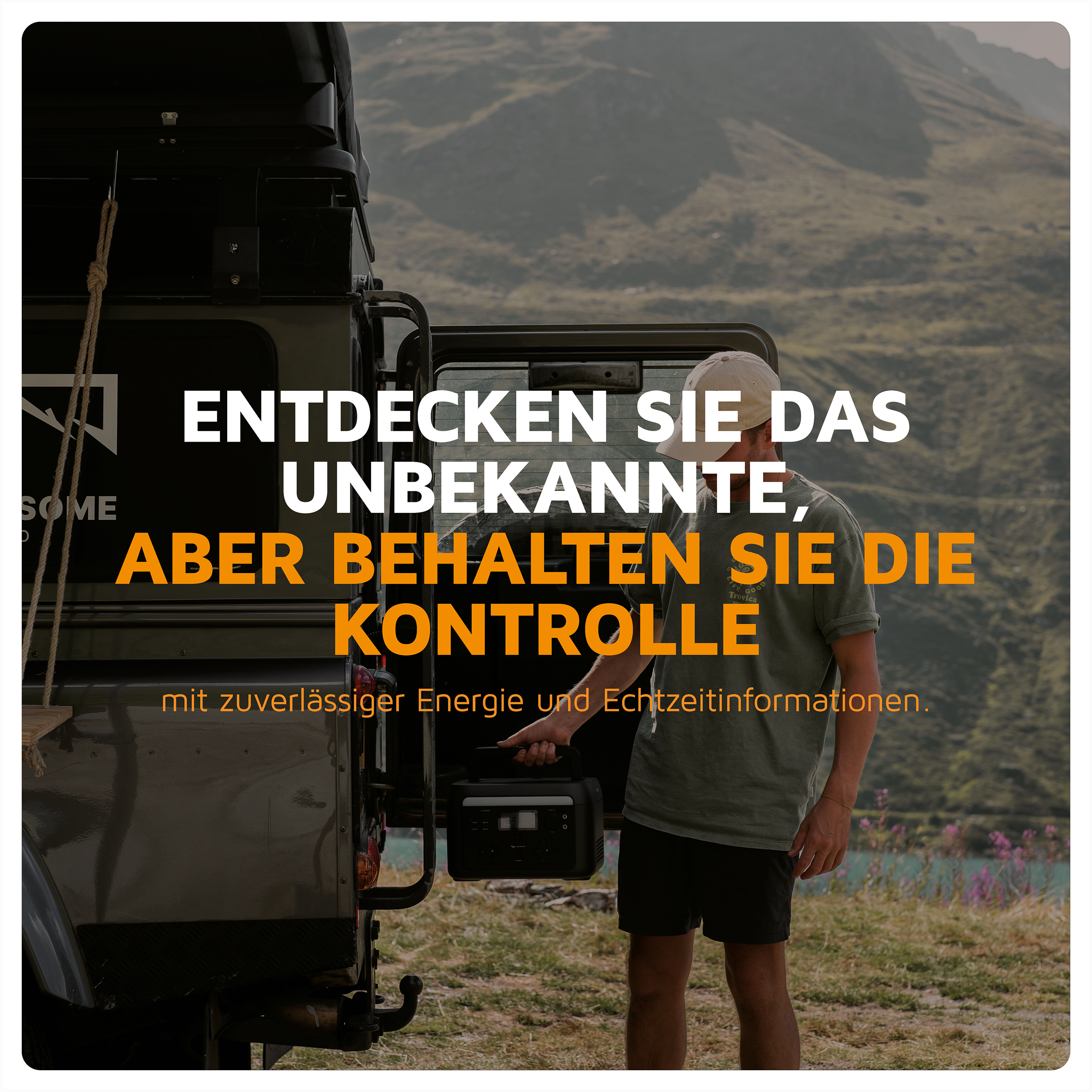 Ein Mann hält eine tragbare Powerstation neben einem robusten Fahrzeug im Freien mit Bergen im Hintergrund.