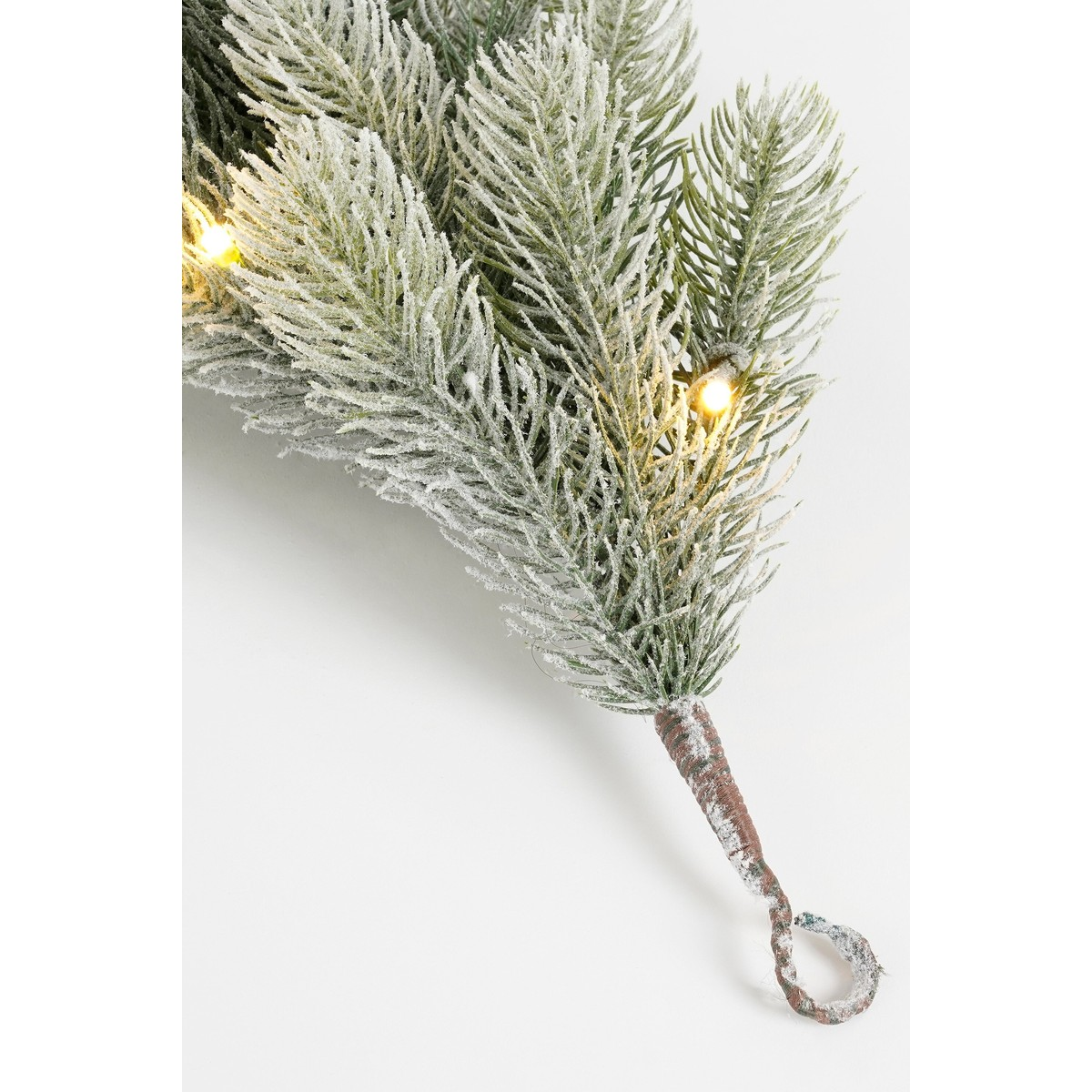 Verschneiter Pinienzweig mit warmen, leuchtenden LED-Lichtern auf weißem Hintergrund.