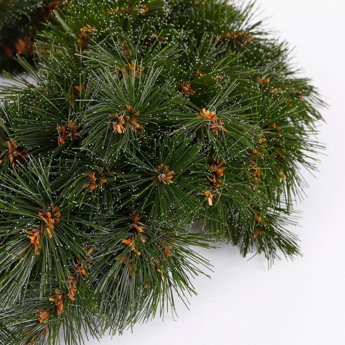 A lush artificial green pine wreath dusted with white snow on a plain white background.