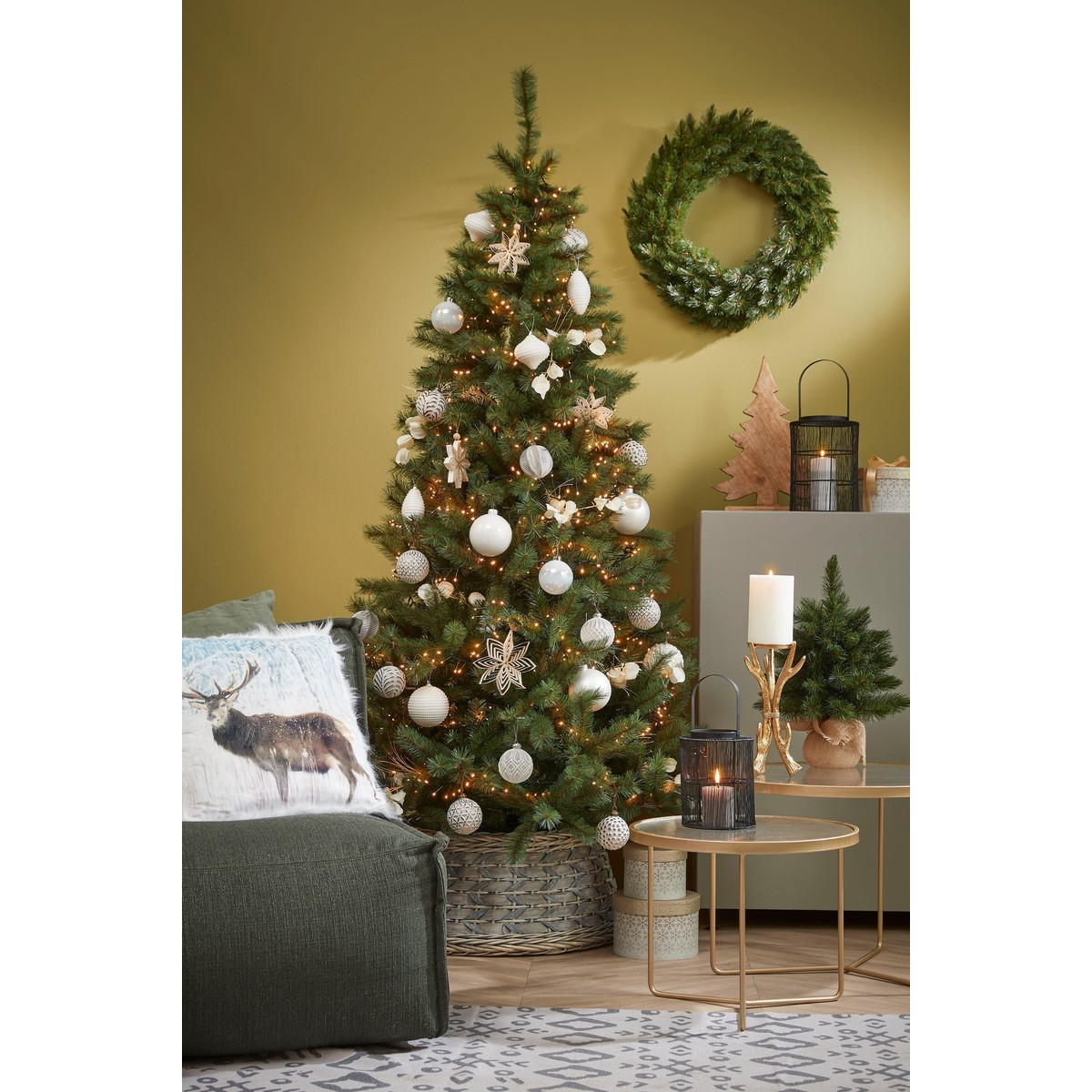 A decorated Christmas tree with white ornaments, lights, a wreath on the wall, and festive side tables with candles.