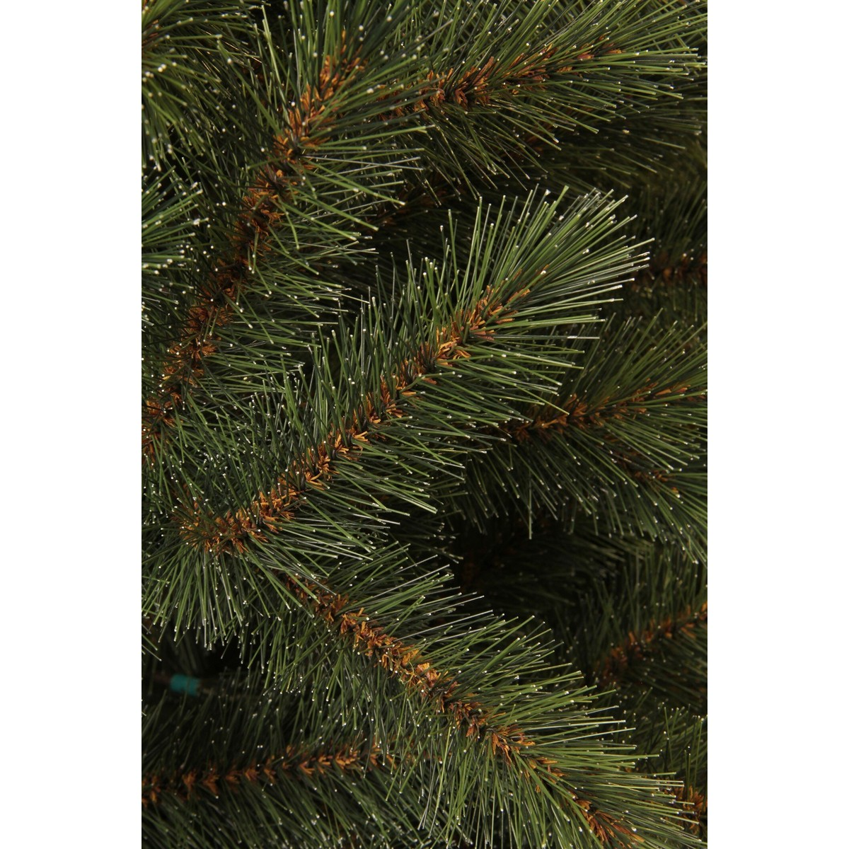 Close-up view of dense green pine needles on brown branches of an artificial Christmas tree.