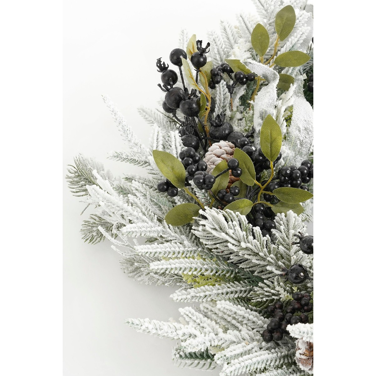 Snow-dusted artificial pine branch with black berries and green leaves.