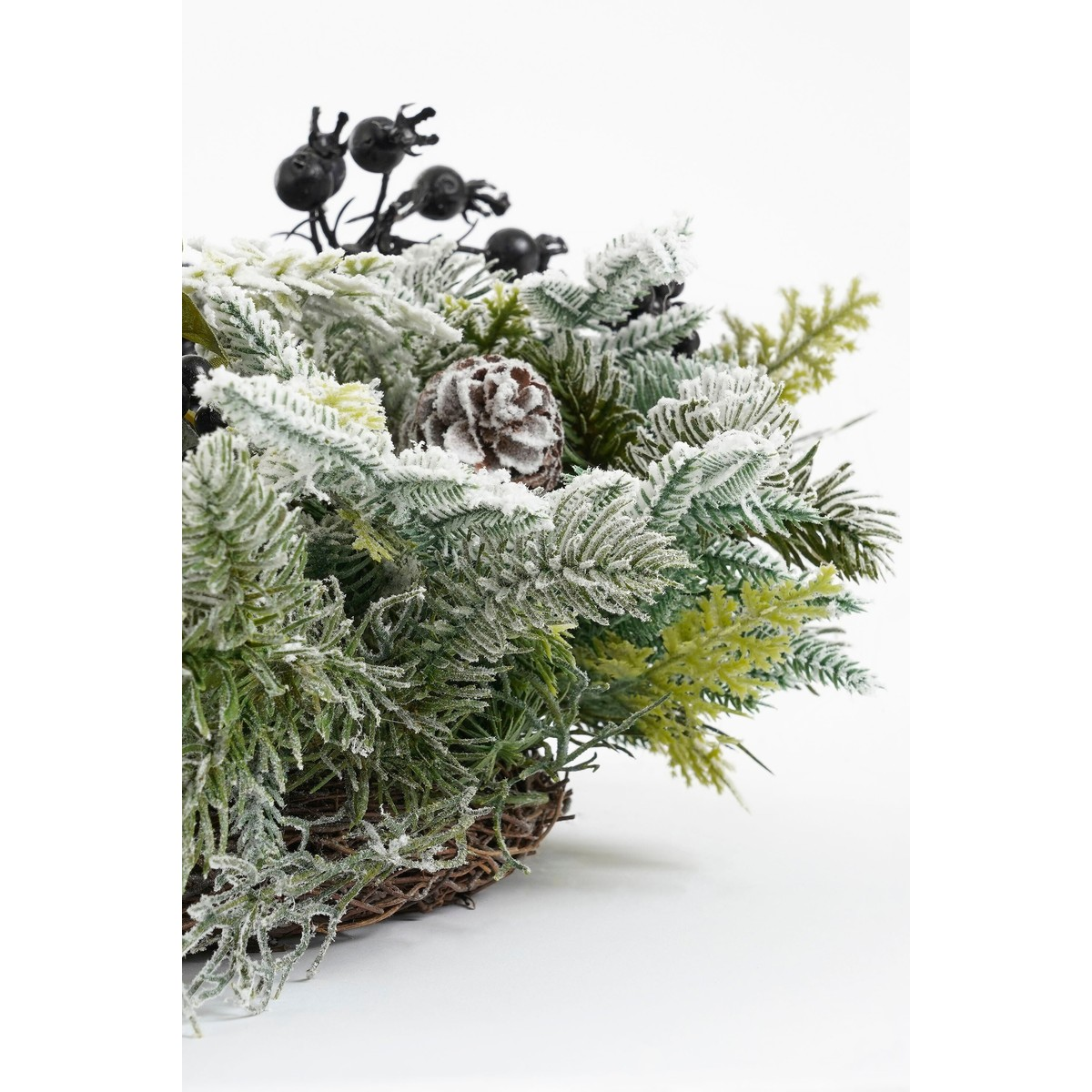 Winter pine branch wreath with artificial snow, pinecone, and black berries on a white background.