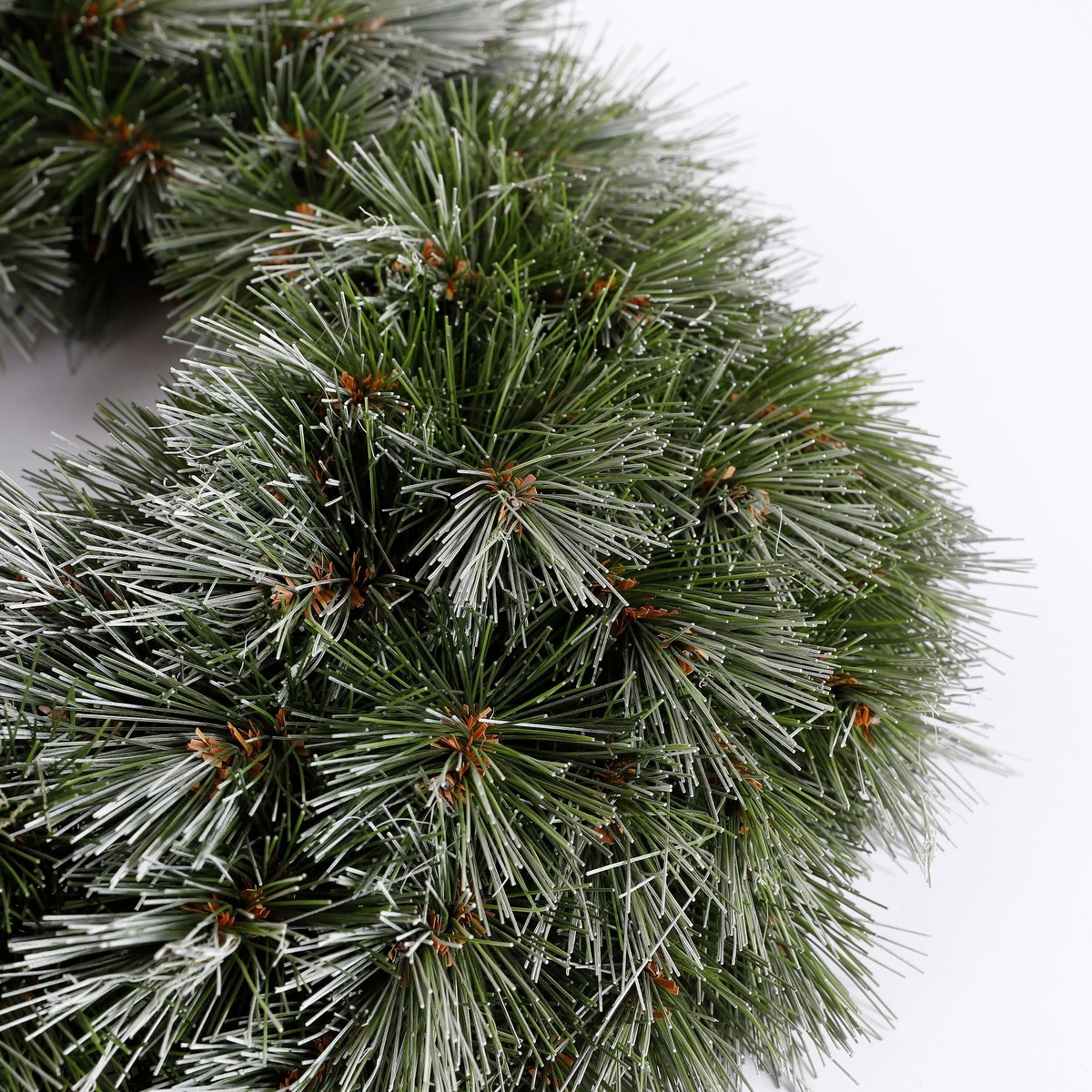 A dense artificial green pine wreath with white-tipped needles on a light background.