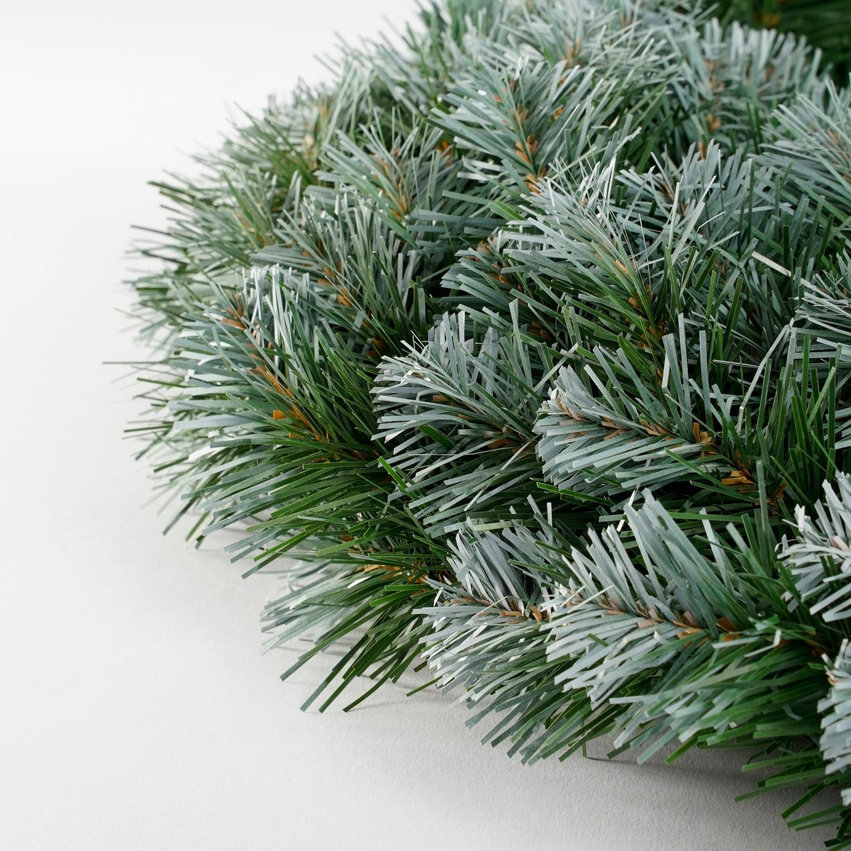 Close-up of a green artificial fir wreath on a white background.