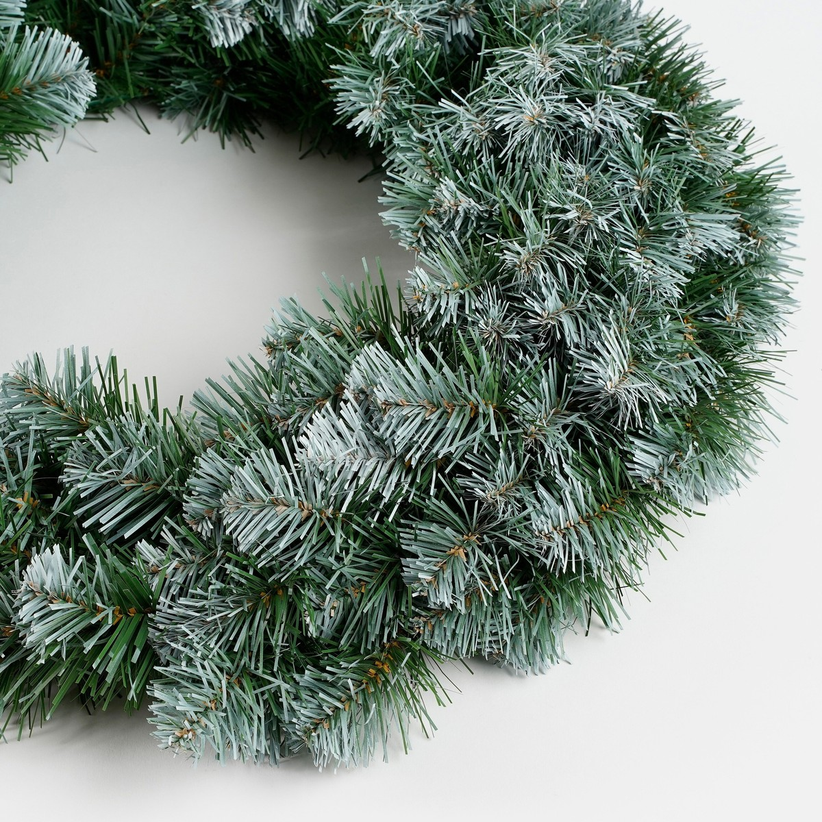An artificial, snow-flocked Christmas wreath made of pine needles on a white background.