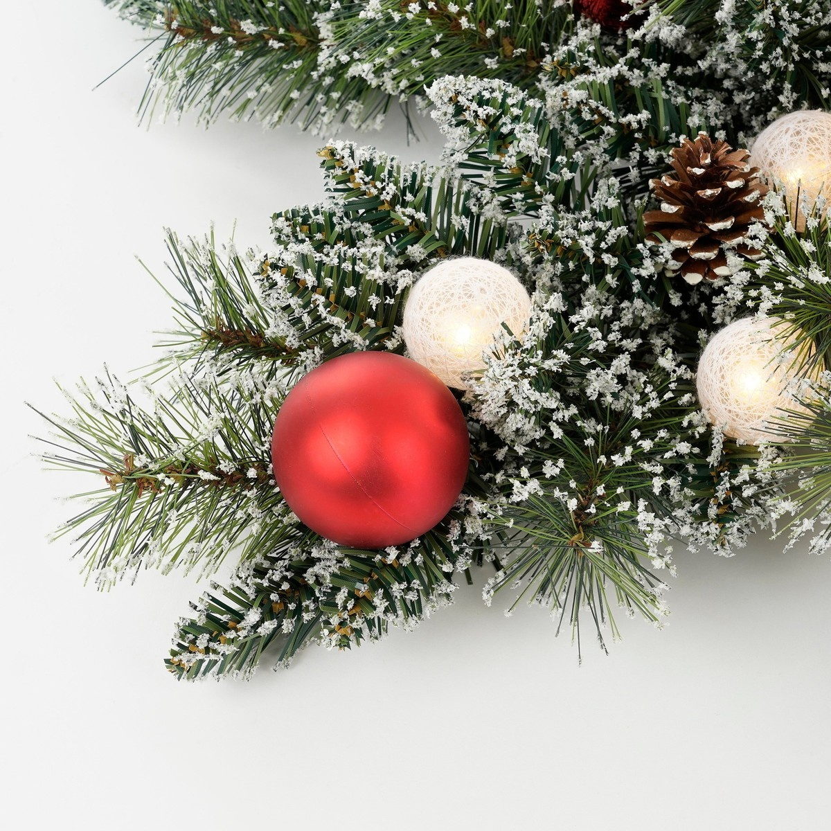 Snowy Christmas tree branch with red ornament, pinecone, and lit spheres.