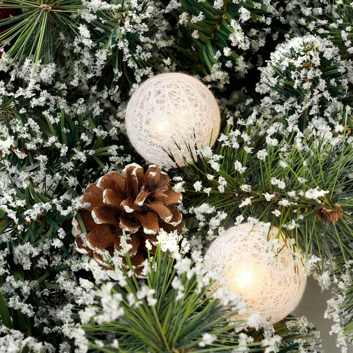 Snow-dusted pine branches, a frosted pinecone, and two glowing string light balls.