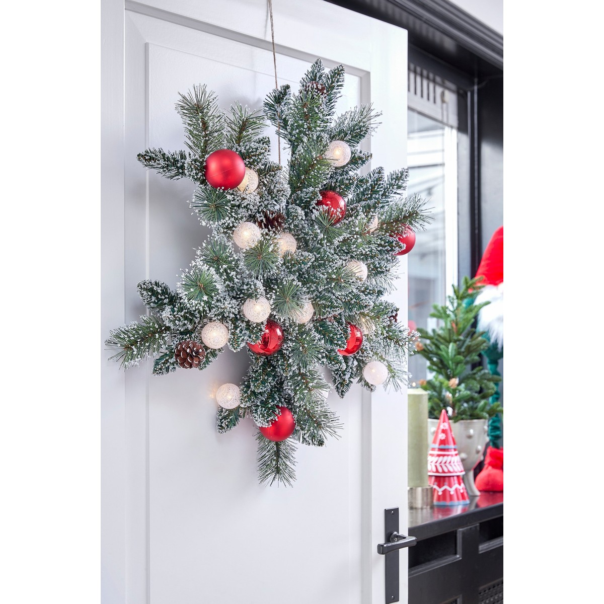 A frosted, star-shaped Christmas branch with red ornaments and lights hangs on a white door.