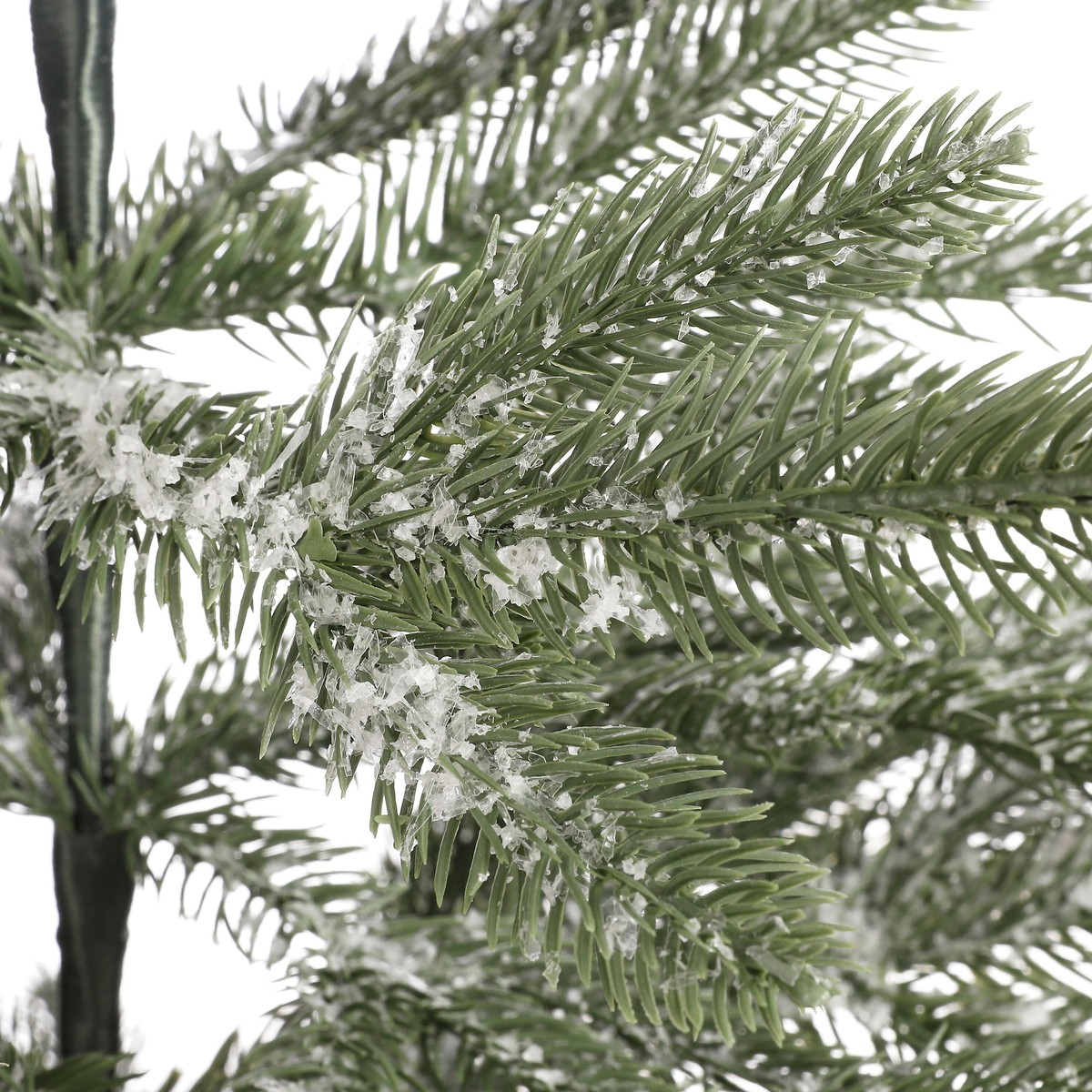 Close-up of green artificial pine tree branches dusted with white snow flakes against a white background.