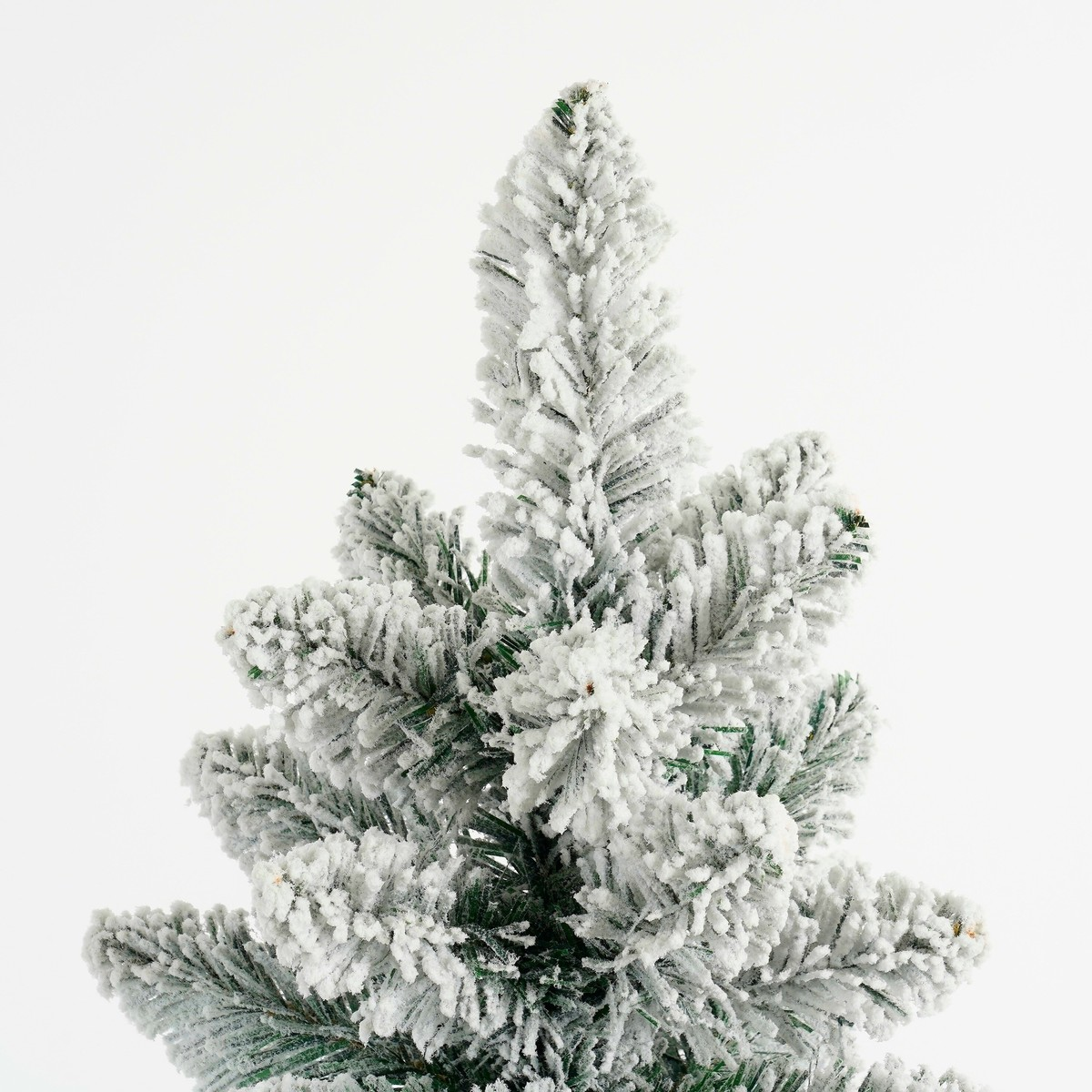Top of an artificial Christmas tree covered with fake snow against a white background.