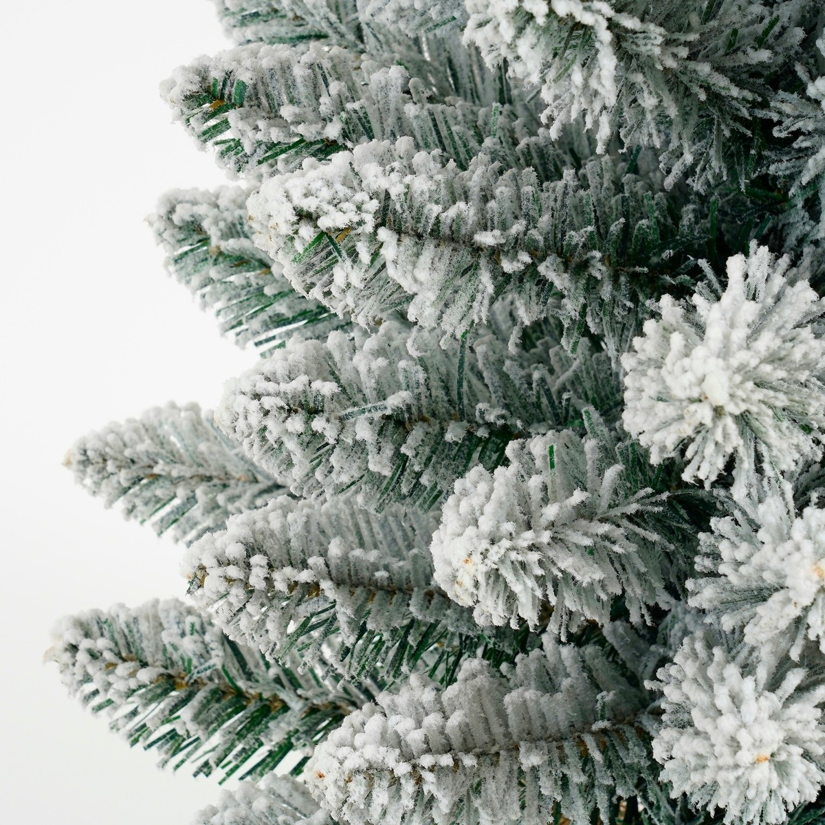 Close-up of artificial green pine tree branches dusted with faux white snow against a plain white background.