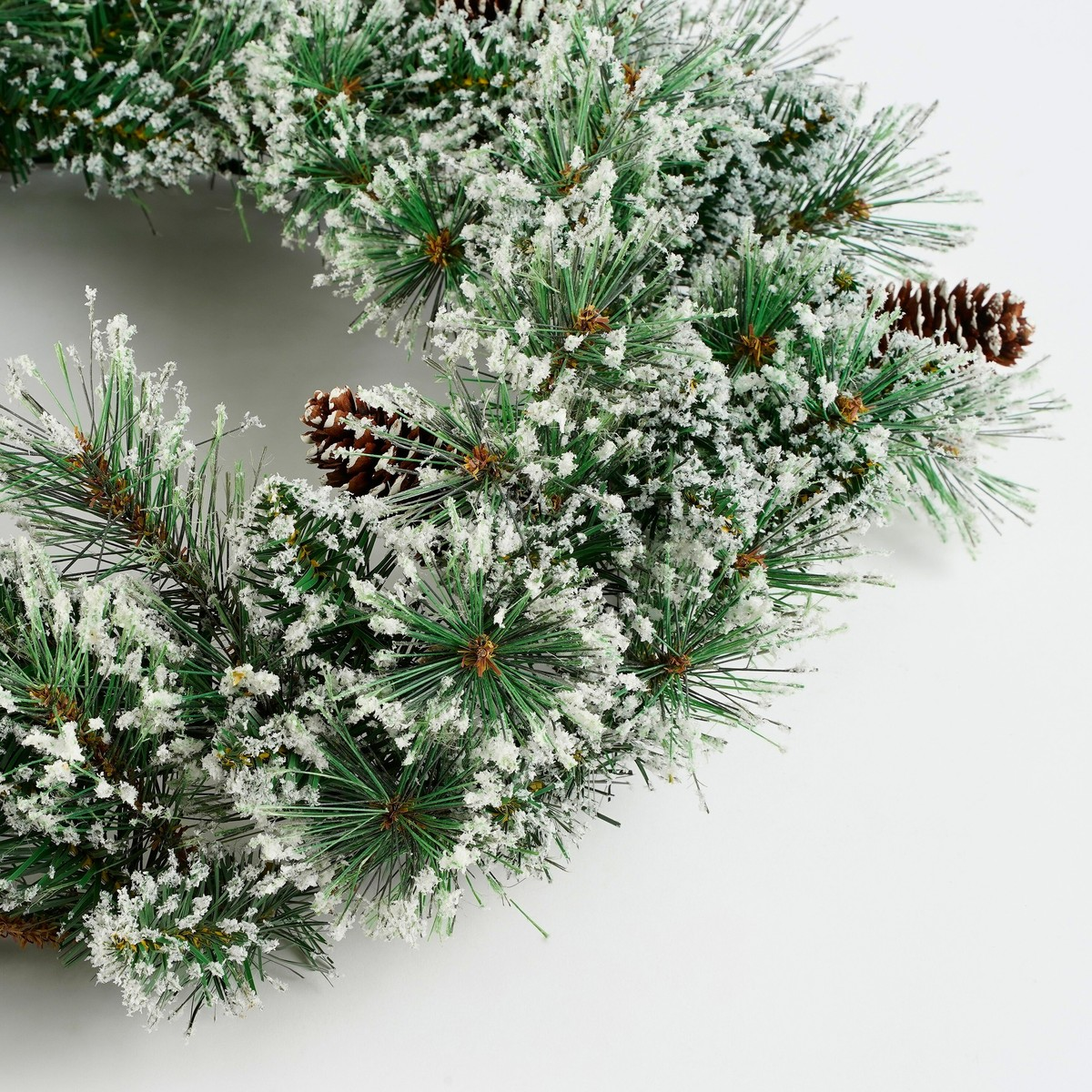 An artificial pine wreath with fake snow and pinecones on a white background.