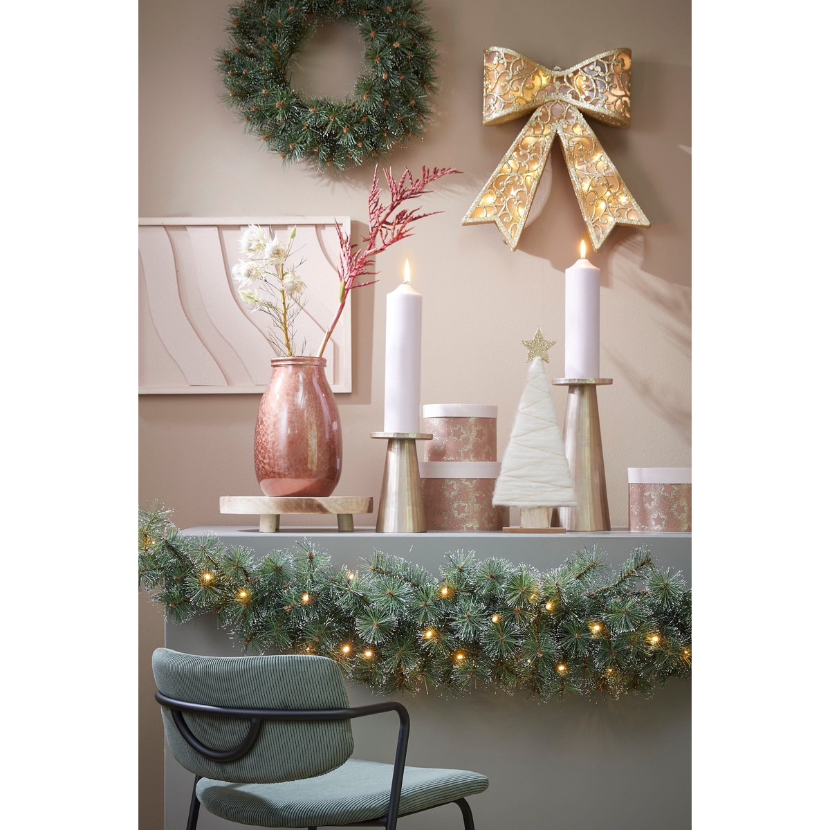 Christmas table decor with candles, gift boxes, illuminated wreath and a bow on the wall.