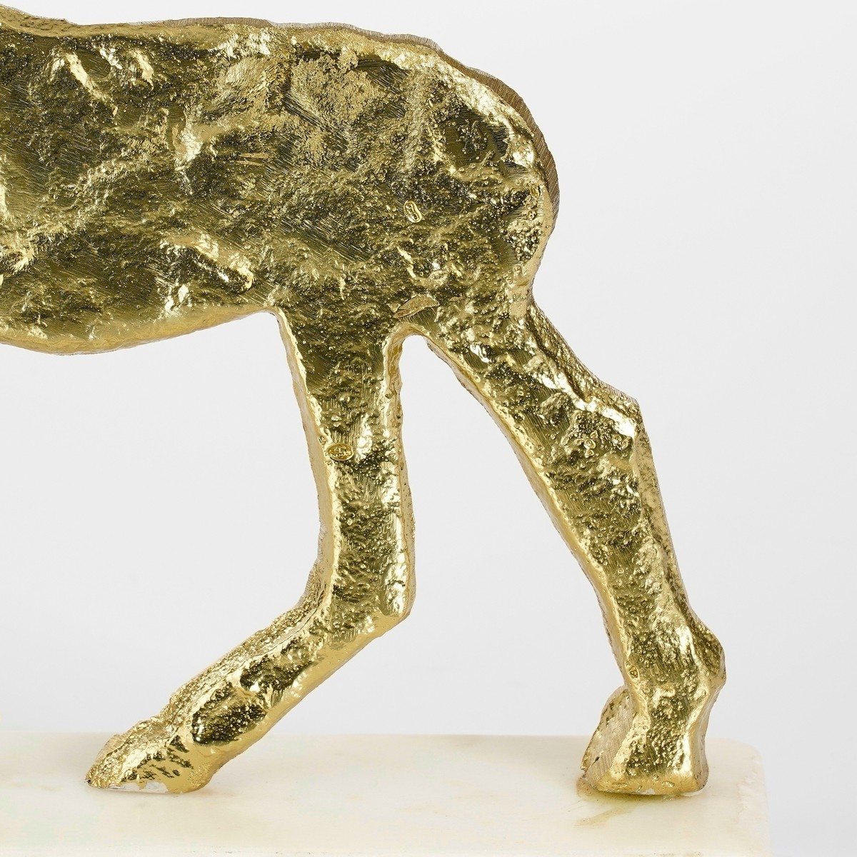 A close-up of a gold-textured animal sculpture's rear legs on a pale base against a white background.