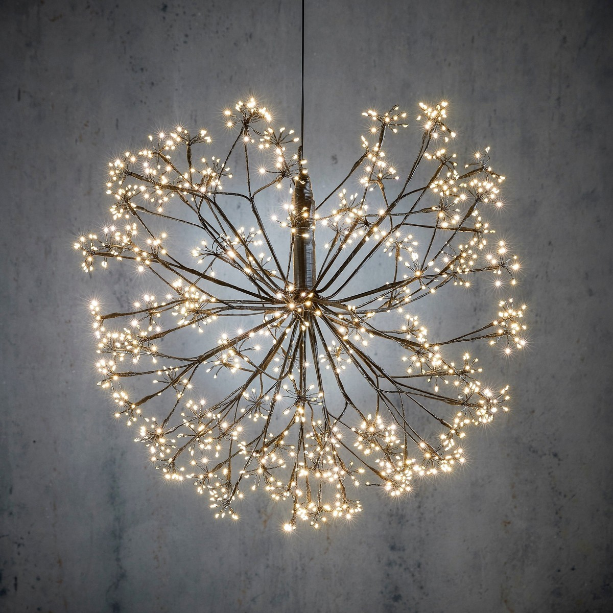 A hanging, spherical light fixture with many tiny lights resembles a dandelion against a grey wall.