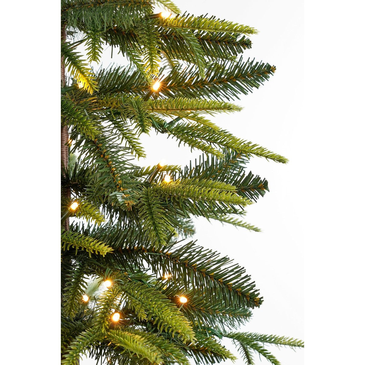 Green branches of an artificial Christmas tree with integrated warm white string lights against a white background.