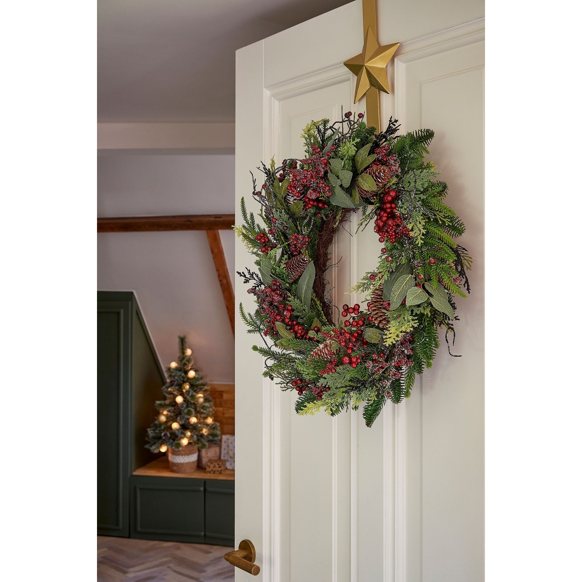 A decorated Christmas wreath with red berries and pinecones hangs on a white door.