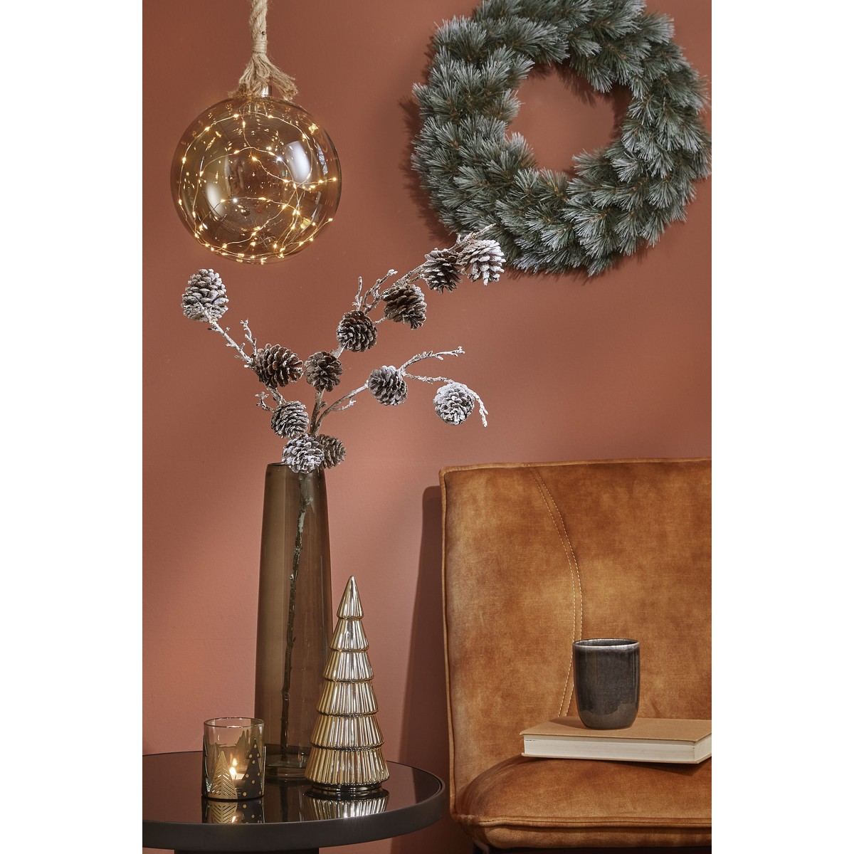 Christmas decor with lit glass ball, wreath, pinecones in vase, and a yellow armchair.