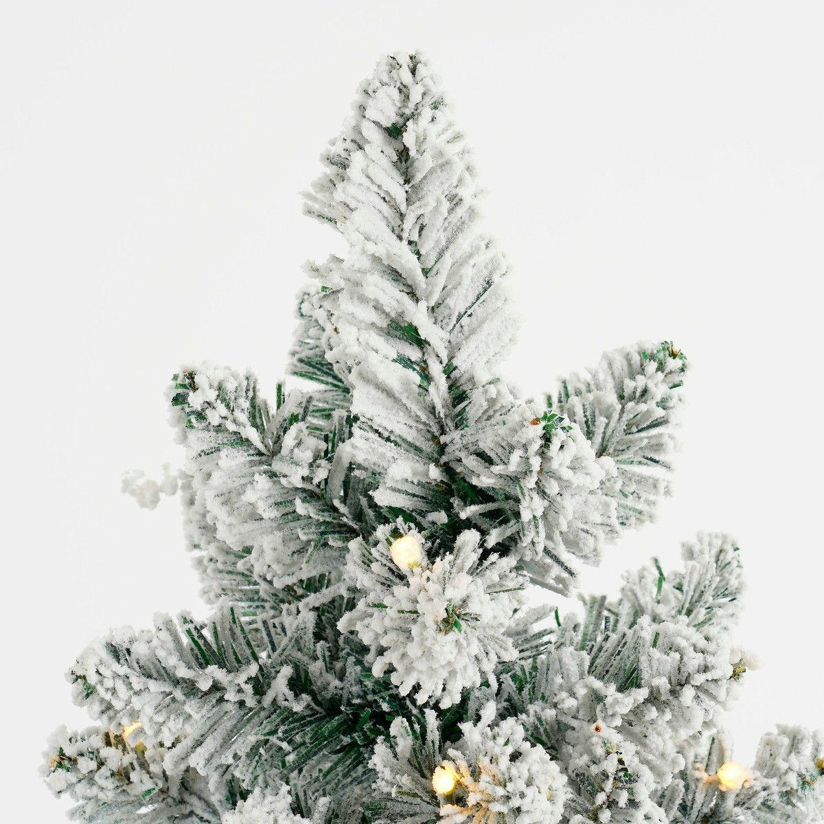 The top half of an artificial Christmas tree covered in snow and small lights.