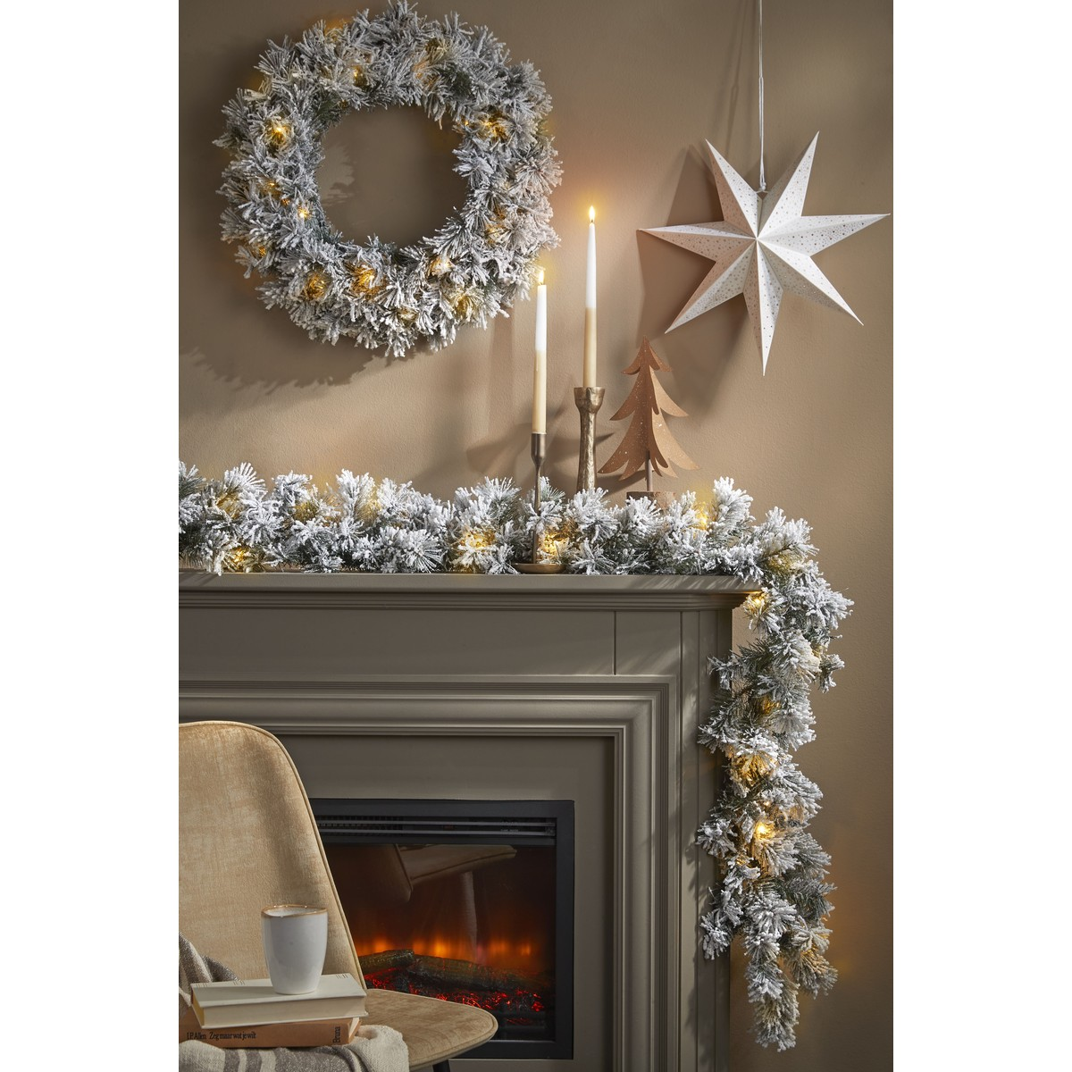 A decorated fireplace mantel with a snowy garland, lit candles, a wreath, and a hanging white paper star.