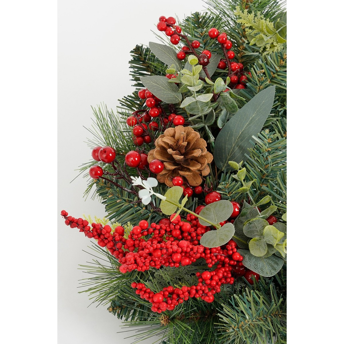 A festive decoration featuring pine needles, red berries, a pinecone, and eucalyptus leaves on a white background.
