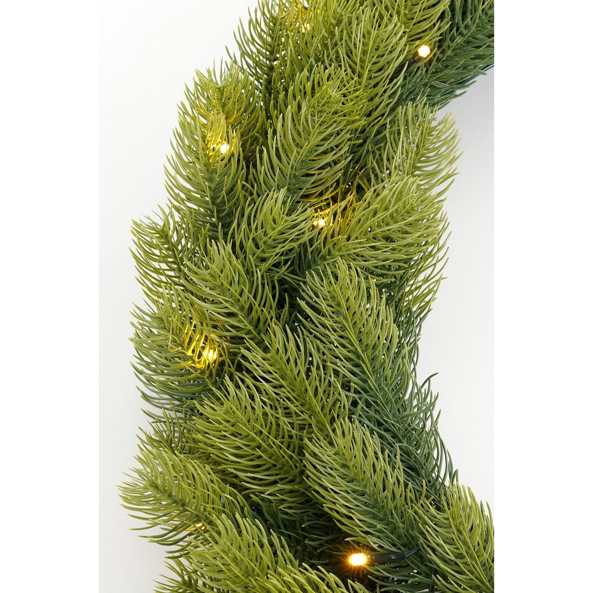 Green artificial fir garland with warm white fairy lights against a white background.