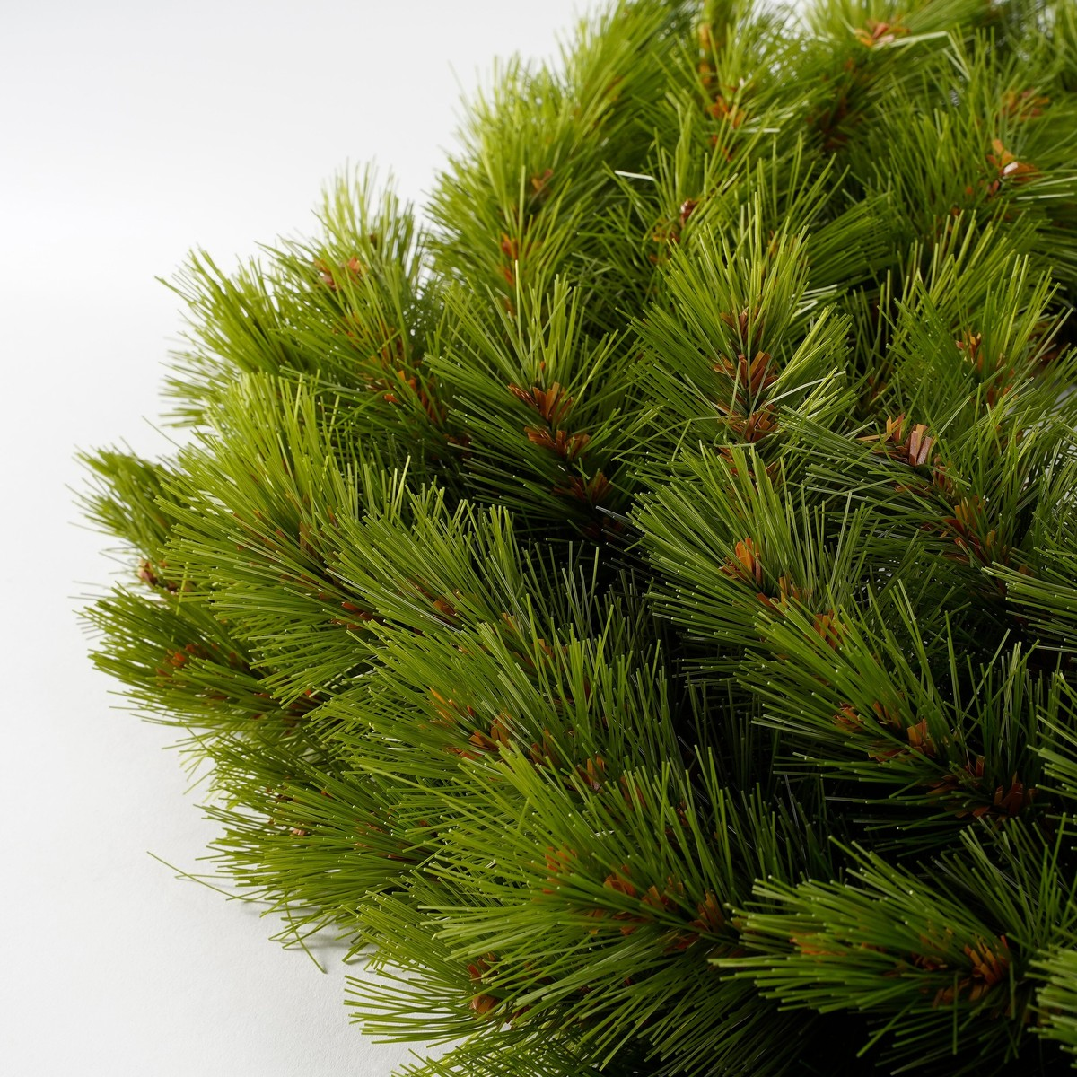 Close-up of artificial green pine branches against a white background.