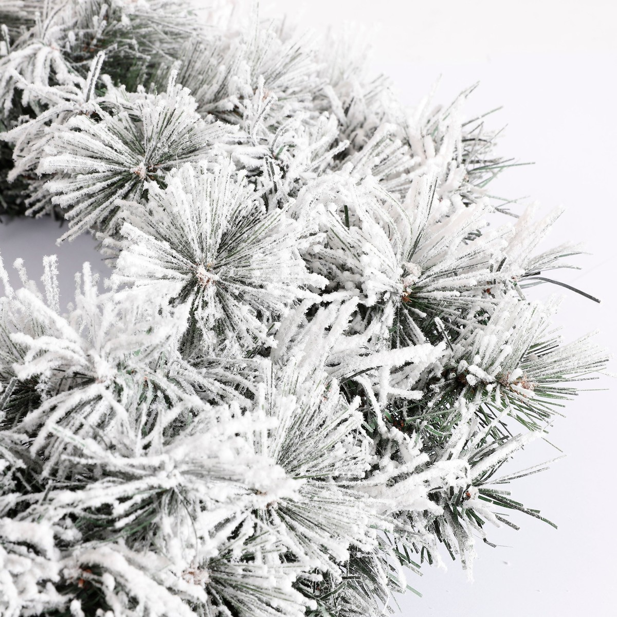 A frosty Christmas wreath with artificial pine needles against a white background.