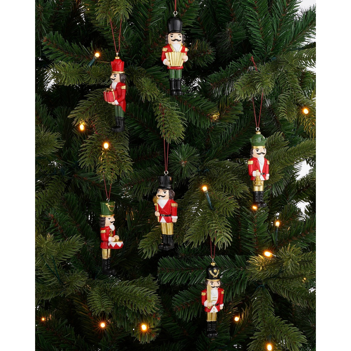 Six nutcracker ornaments hang on a green Christmas tree illuminated with small lights.