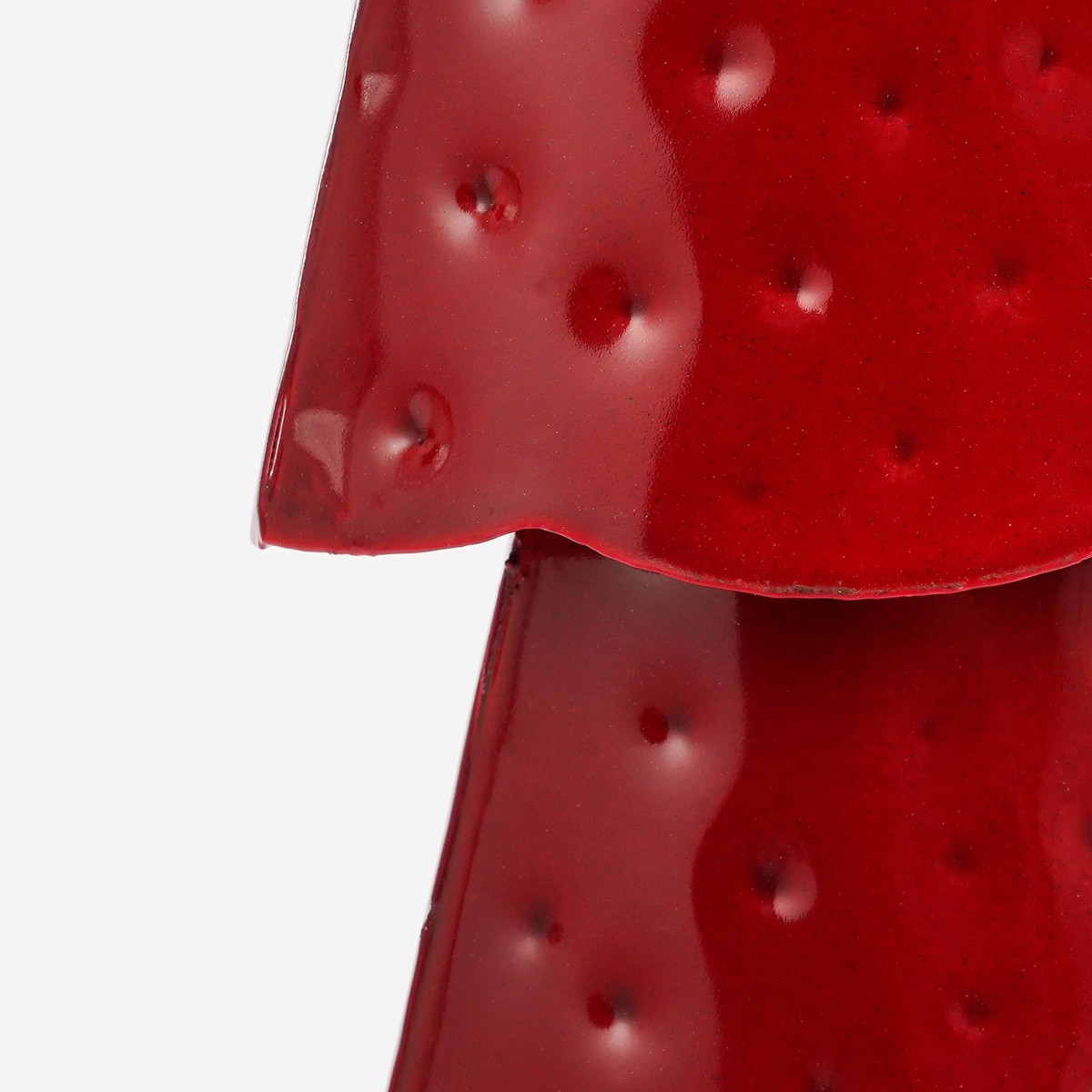 Glossy red metal mushroom with indented dots on a white background.