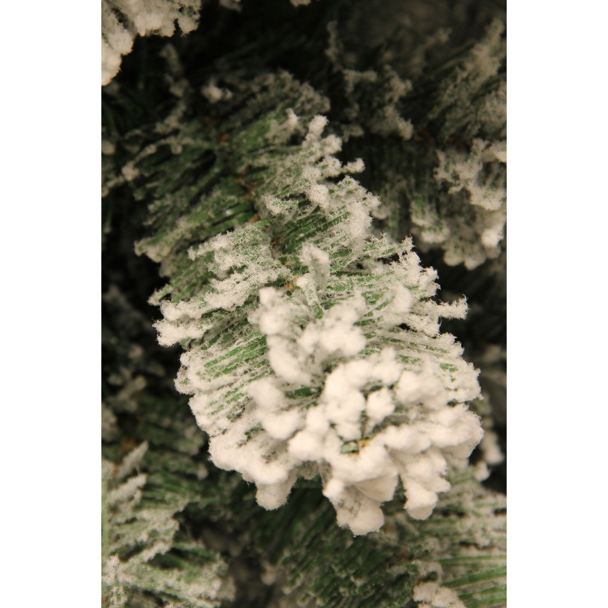 Close-up of a green artificial Christmas tree branch covered in fake snow.
