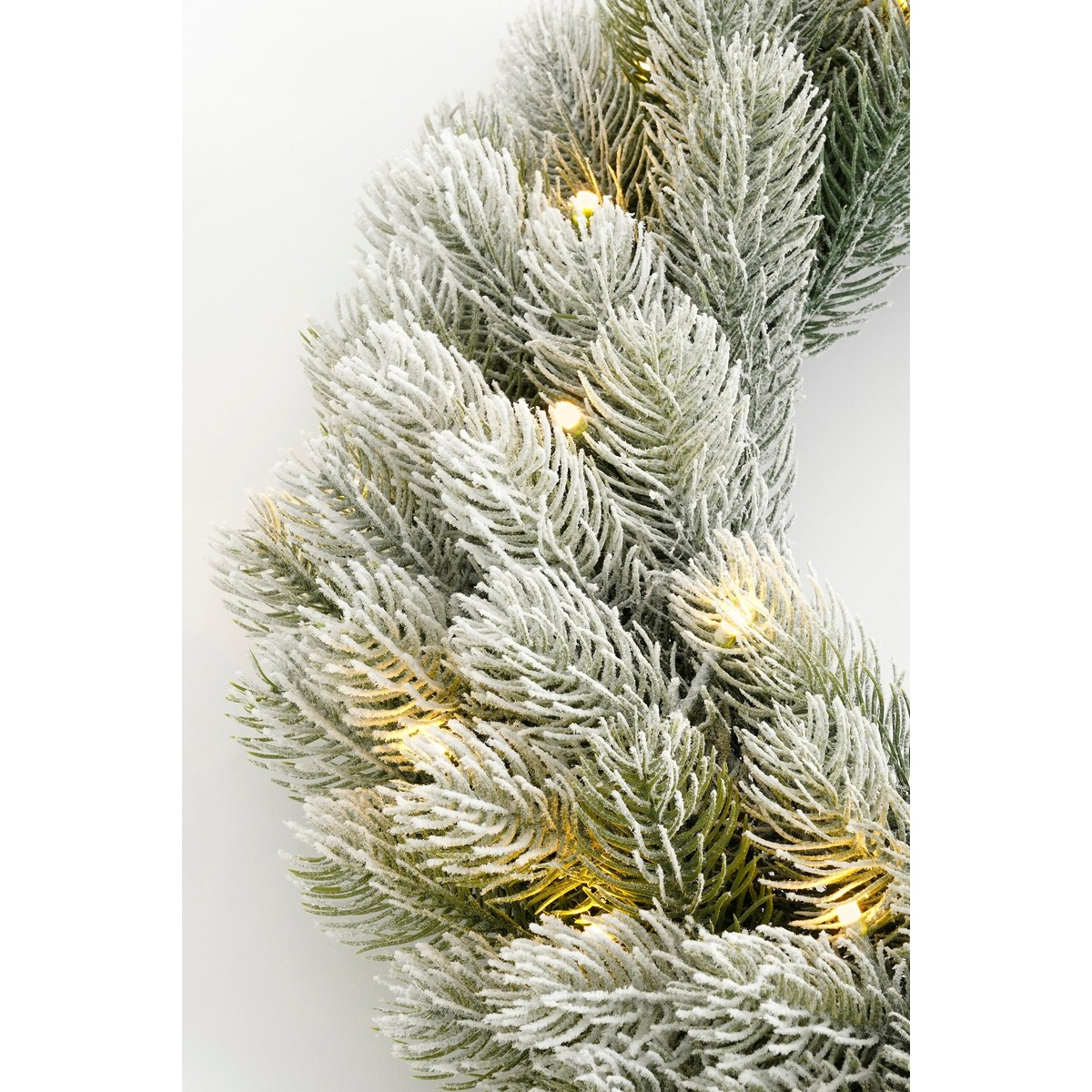 Snow-covered artificial fir branch with warm LED lights on a white background.