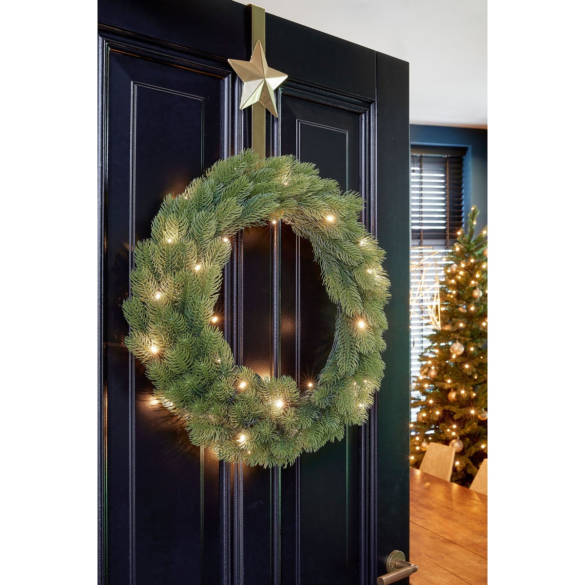 A lit green Christmas wreath with a gold star hangs on a black door.
