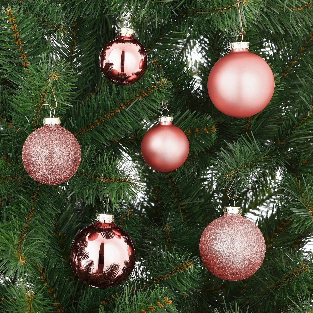 Pink Christmas baubles with glossy and matte finishes hanging on green pine branches.
