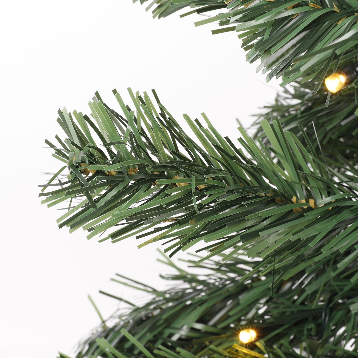 Artificial green Christmas tree branches with small bright lights against a white background.