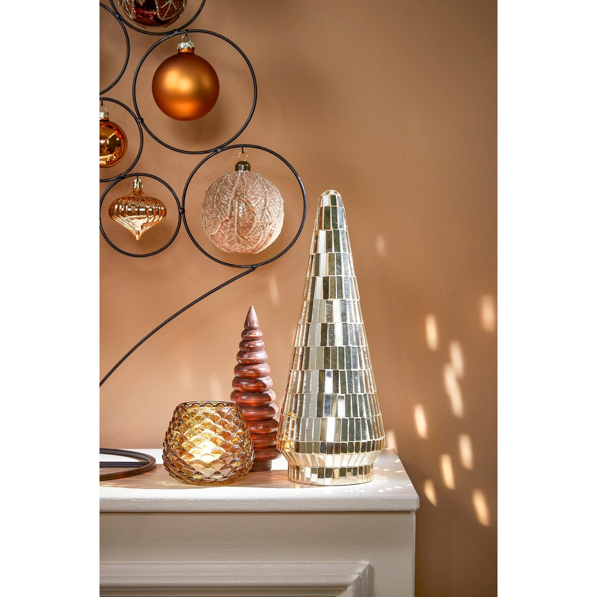 Golden Christmas decor includes a mosaic tree, a ribbed tree, a lit candle holder, and hanging baubles.
