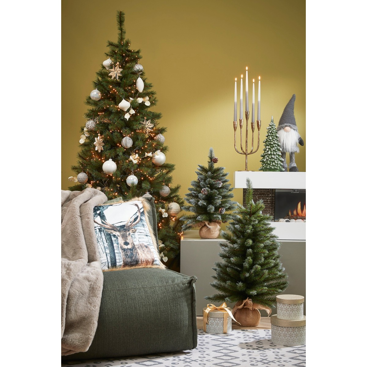 A decorated Christmas room with a large tree, small trees, a deer cushion on an armchair, gifts, and a gnome.
