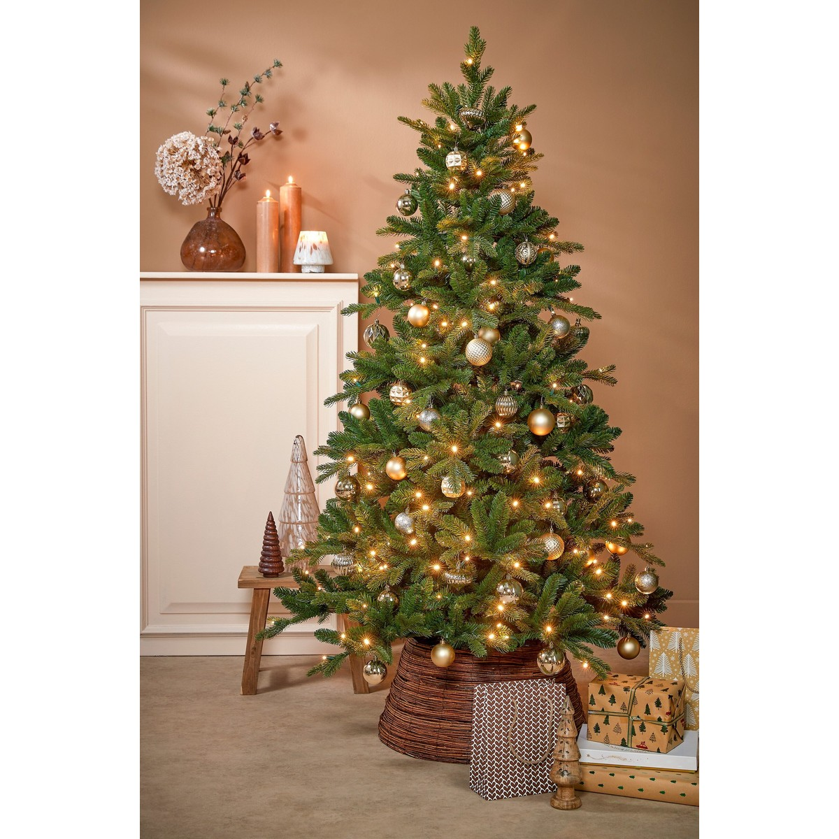 A decorated Christmas tree with lights and gold ornaments stands before a beige wall with gifts.