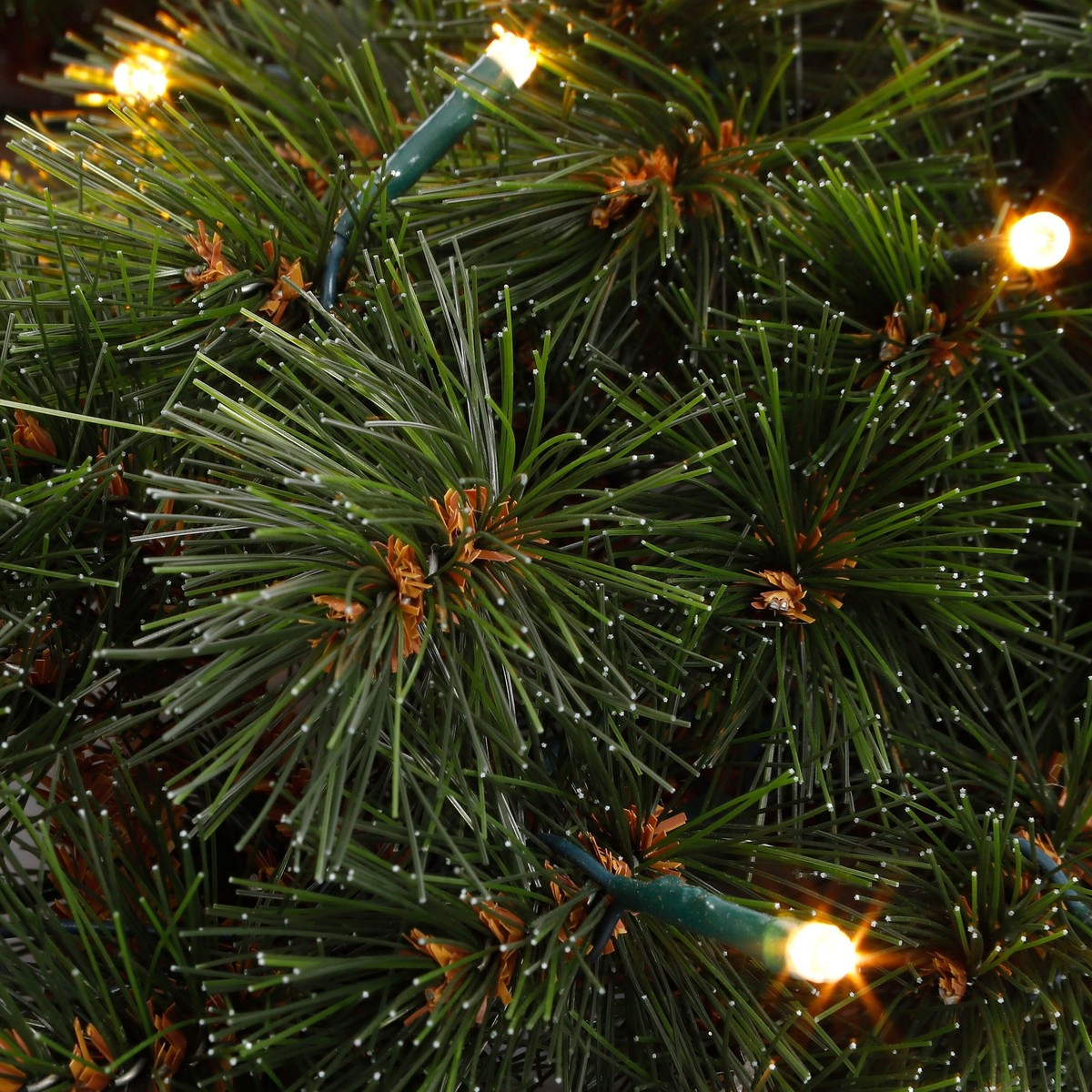 Green artificial pine branches with white tips and glowing Christmas lights.