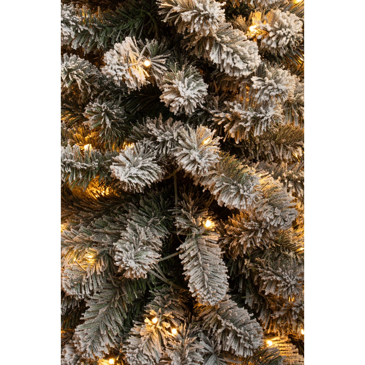 Close-up of an artificial Christmas tree covered in snow and warm lights.