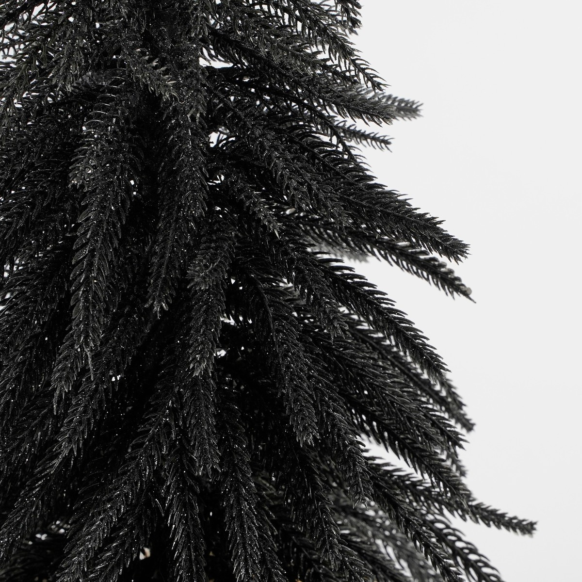 Close-up of an artificial black Christmas tree with glittering needles against a white background.