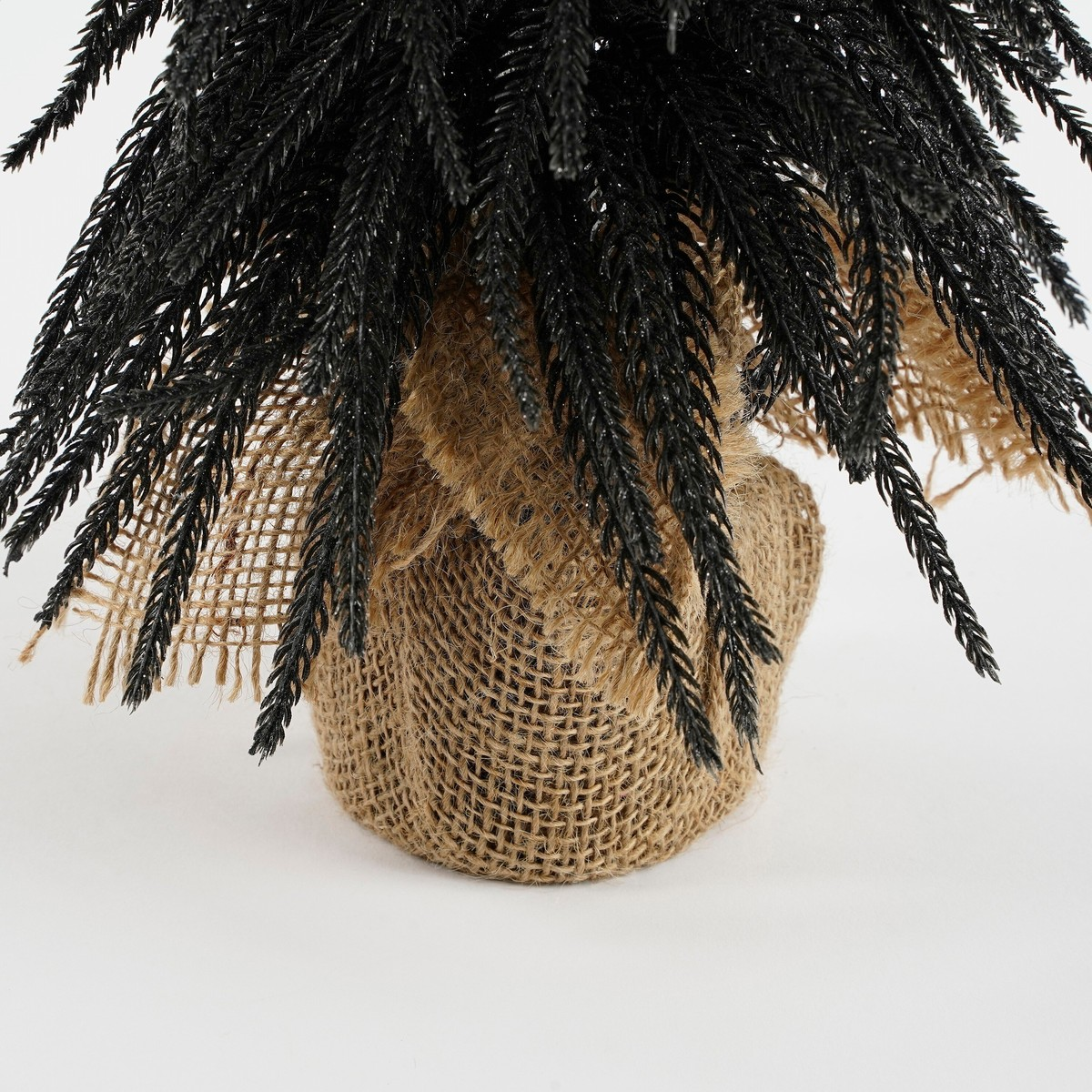 A small artificial black glitter tree in a burlap sack against a light background.