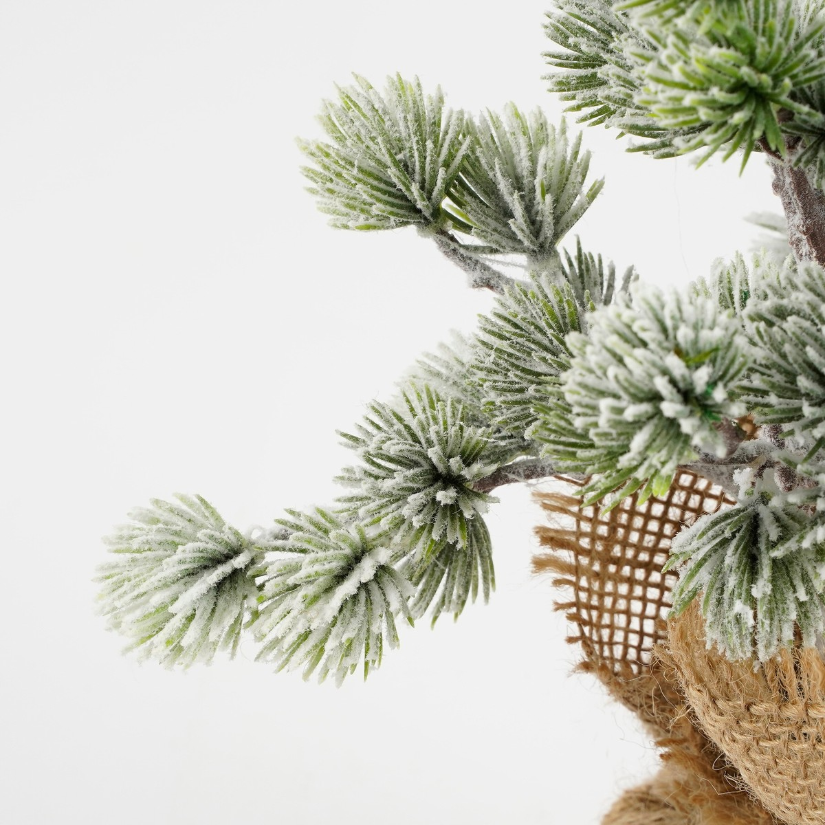 Artificial, snow-covered pine branch in a burlap sack against a white background.