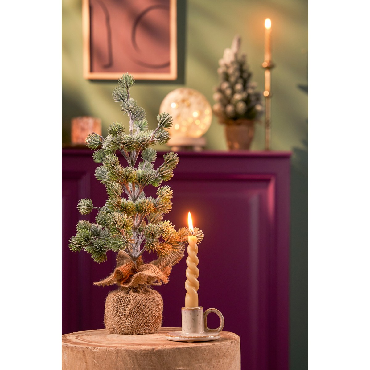 Small artificial pine tree in burlap and a lit candle stand on a wooden block.