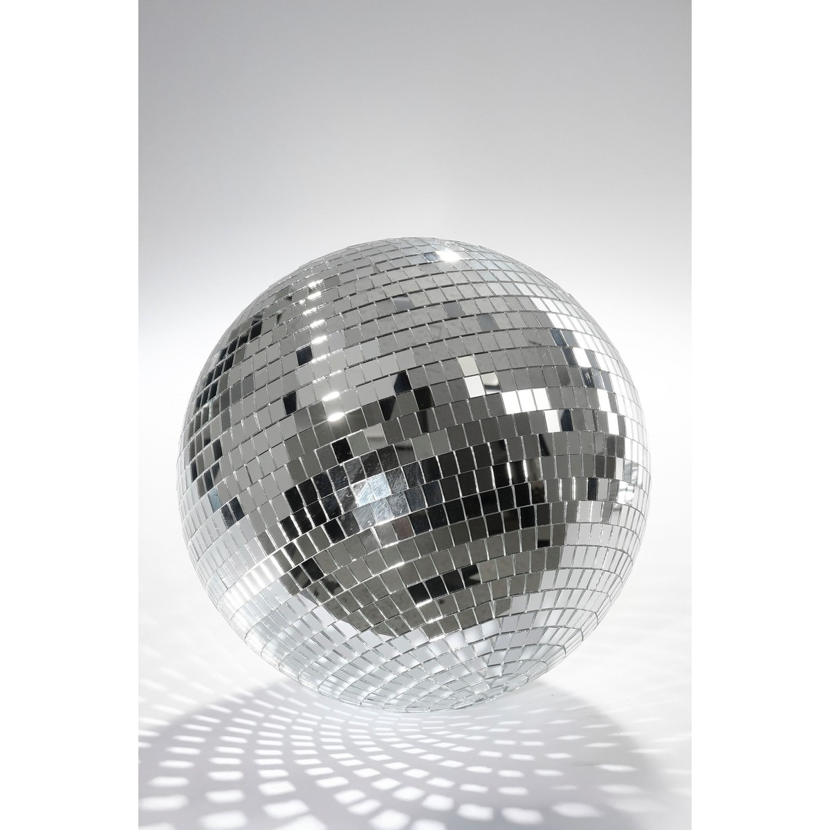 Une boule à facettes argentée et brillante avec de petits miroirs repose sur une surface blanche, projetant des motifs.