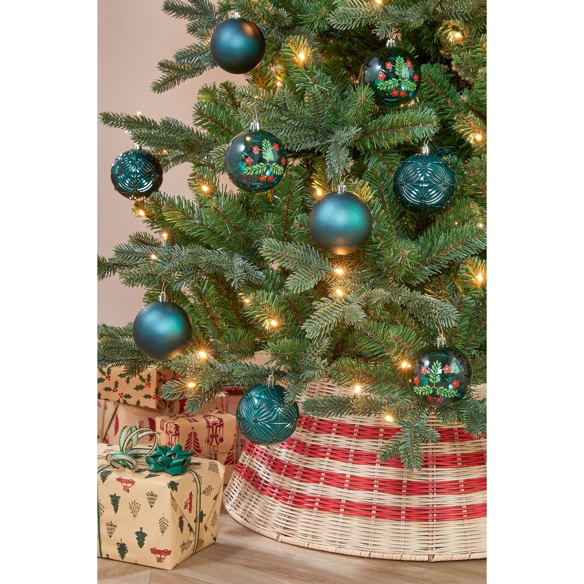 Christmas tree decorated with blue ornaments and lights, with gifts and a woven tree collar below.