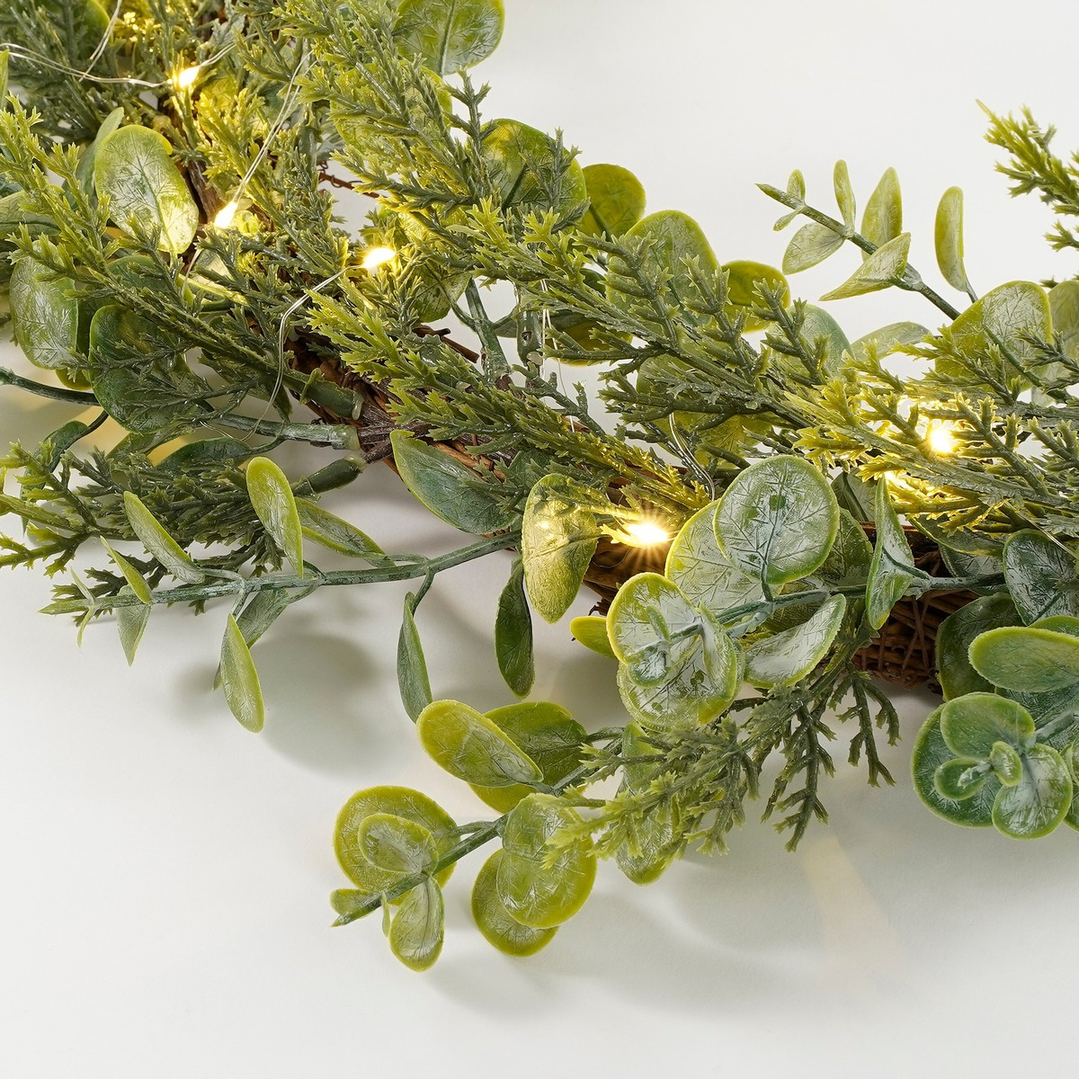 Green artificial eucalyptus garland with warm fairy lights on a white background.