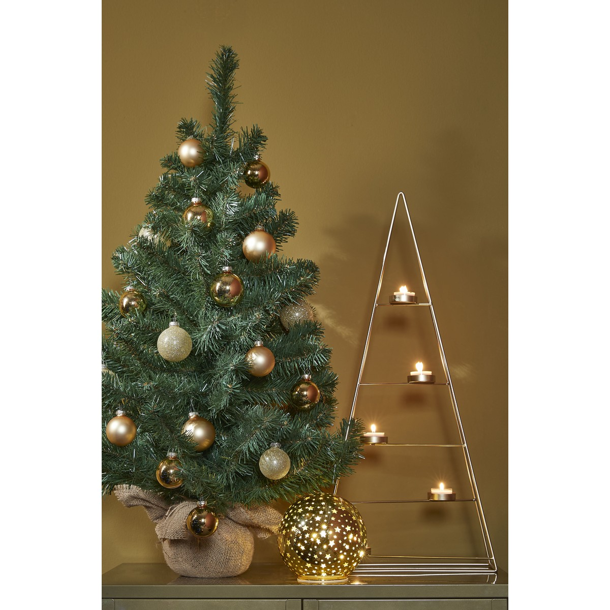 Small Christmas tree with gold baubles, a triangular candleholder structure, and a glowing globe on a table.