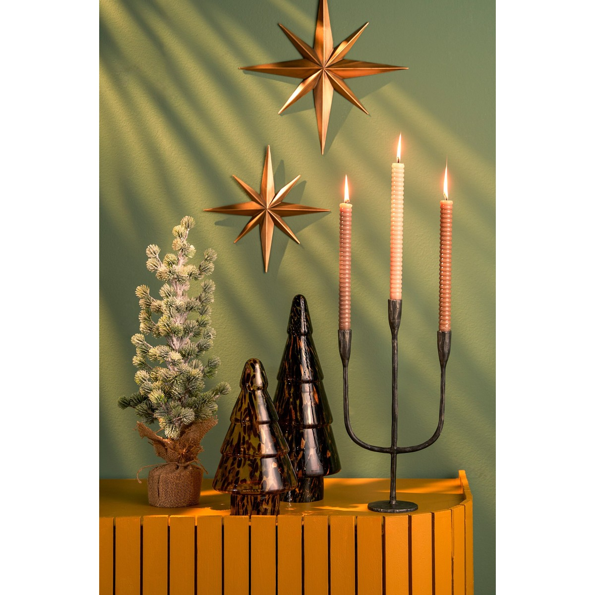 Holiday display with small trees, a candelabra, and golden stars on a green wall.